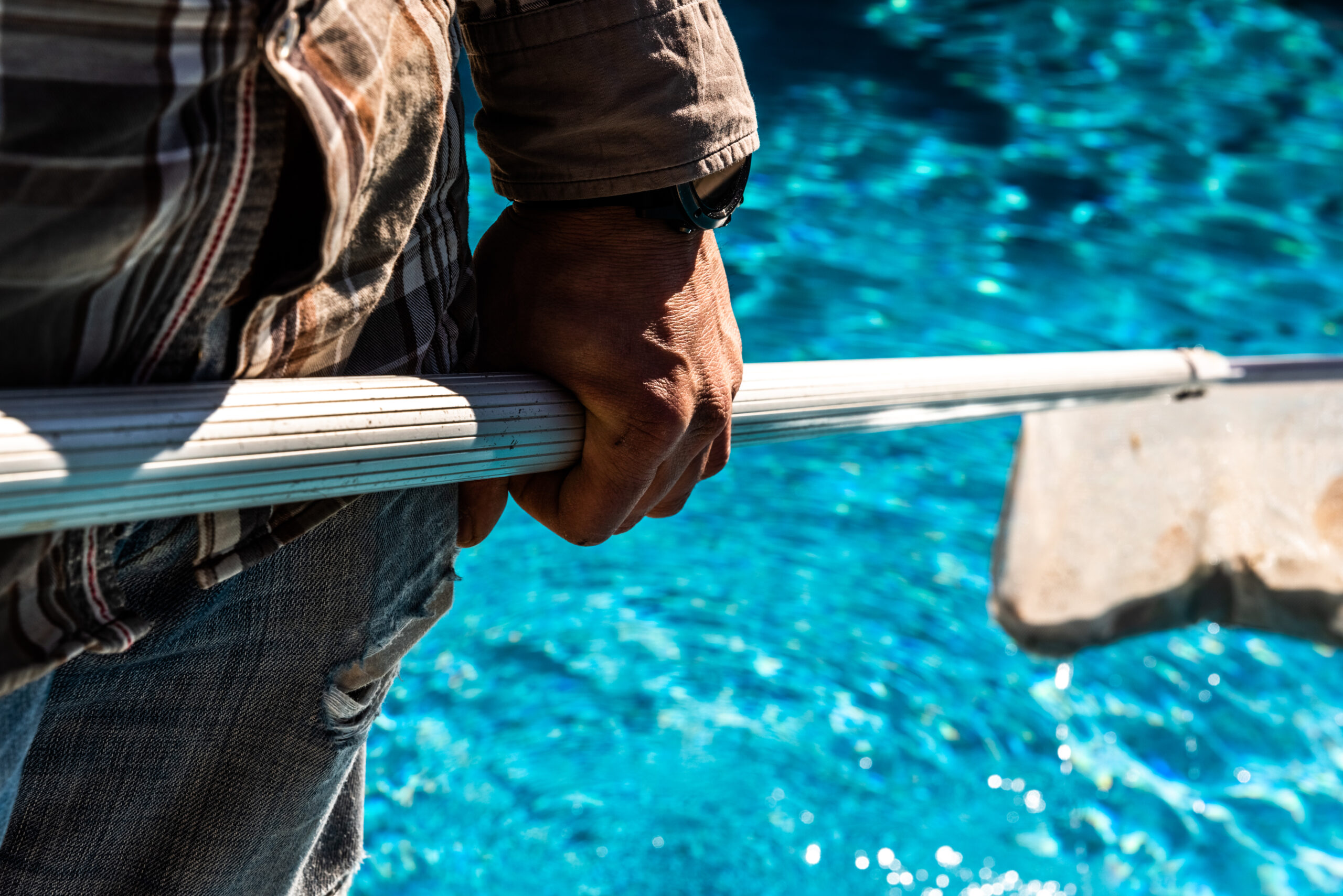 Personne utilisant une épuisette pour l'entretien de piscine et éviter les erreurs d'accumulation de débris - Erreurs en entretien de piscine