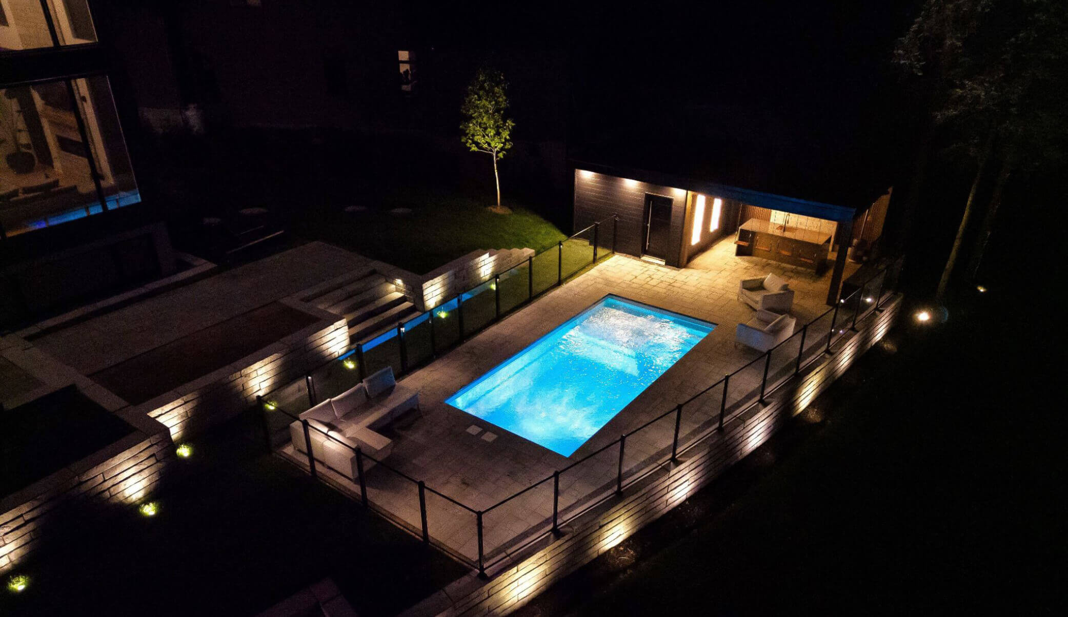 Éclairage paysager mettant en valeur une piscine creusée illuminée et des murets de pierre la nuit