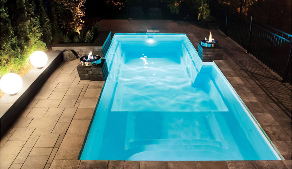 Éclairage paysager avec lampes sphériques et foyers au gaz autour d'une piscine creusée éclairée