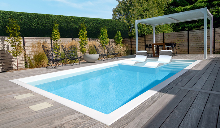 Tendances de piscine en 2026 : piscine rectangulaire moderne avec pergola blanche et terrasse en bois gris