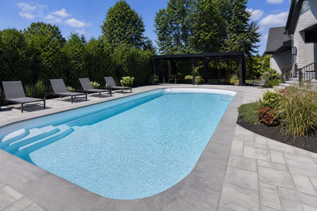 Entretien d'une piscine en fibre de verre bien réalisé : bassin à l'eau turquoise cristalline entouré d'un aménagement paysager soigné