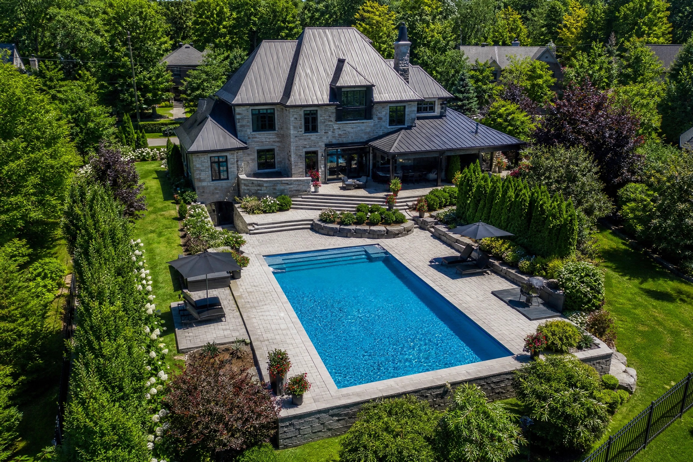 Vue aérienne d'une résidence en pierre avec bassin creusé, terrasse en pavé et aménagement paysager haut de gamme, un bel exemple de la valeur ajoutée d'une piscine à une propriété